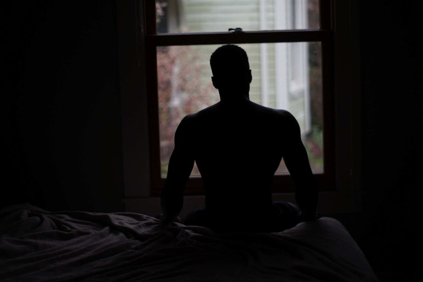 Silhouette of a man sitting on the bed looking at daylight outside