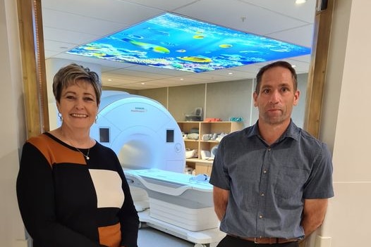 A man and a woman stand in front of an MRI machine.