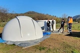 white dome observatory in paddock surrounded by men