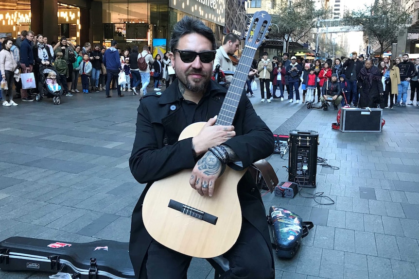A tattooed man on the street holding a guitar