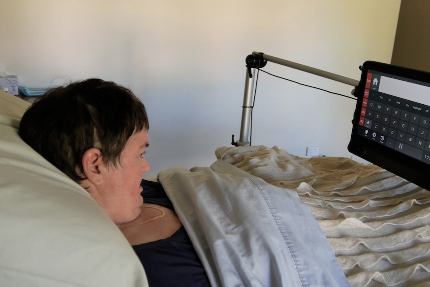 A woman in bed with a screen in front of her. There are letters on the screen keyboard.