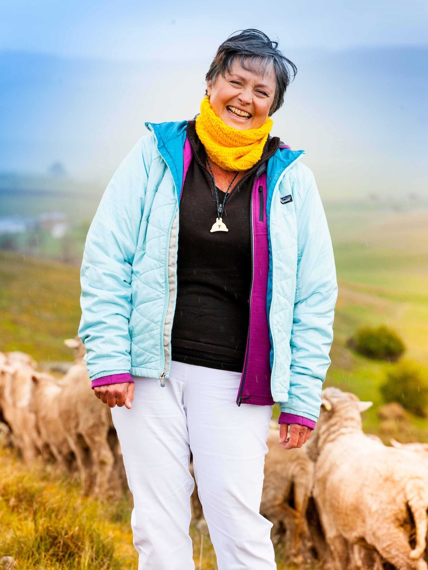 An older woman in bright winter clothing laughs in a paddock.