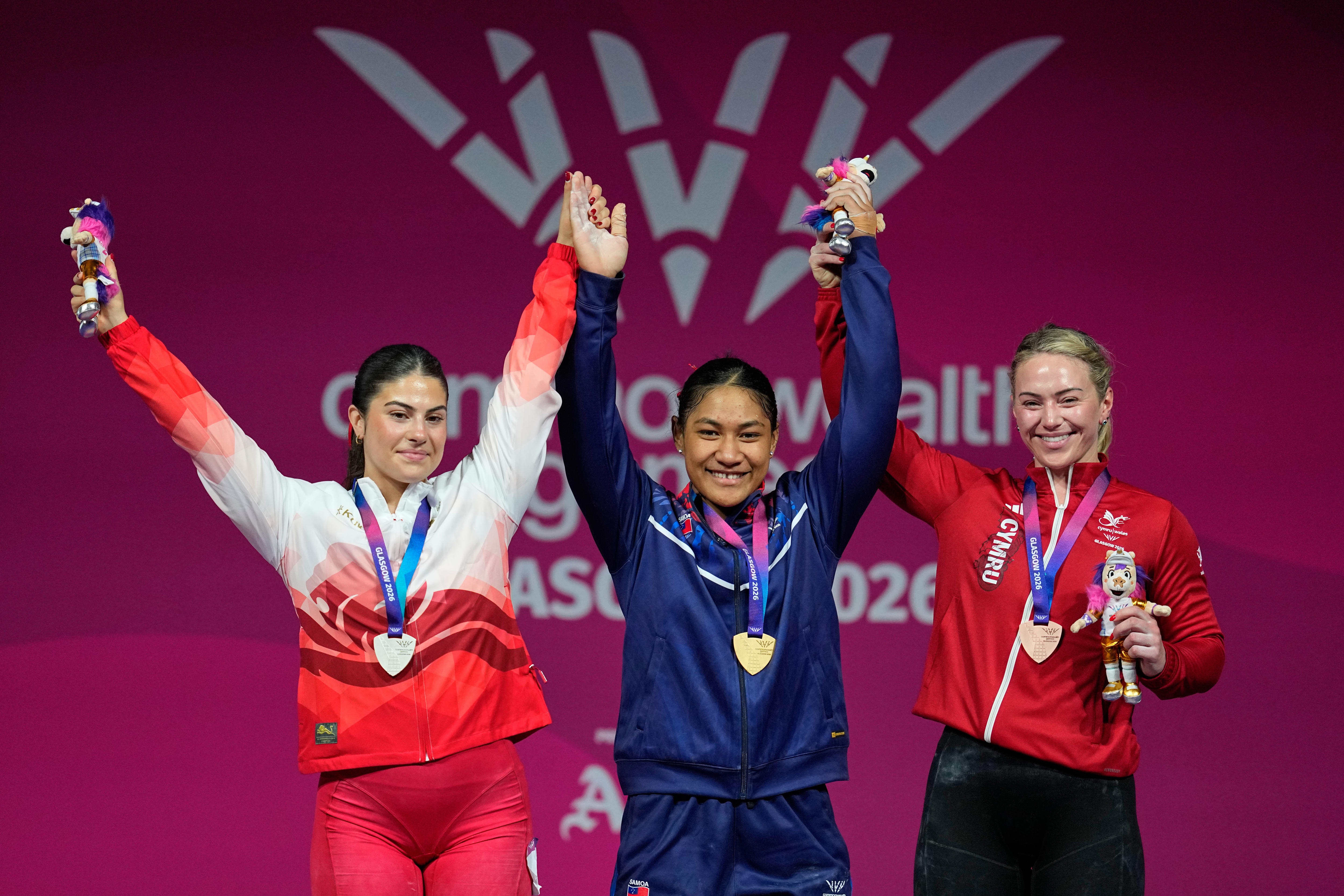 Three women stand on a podium, all wearing medals and smiling.