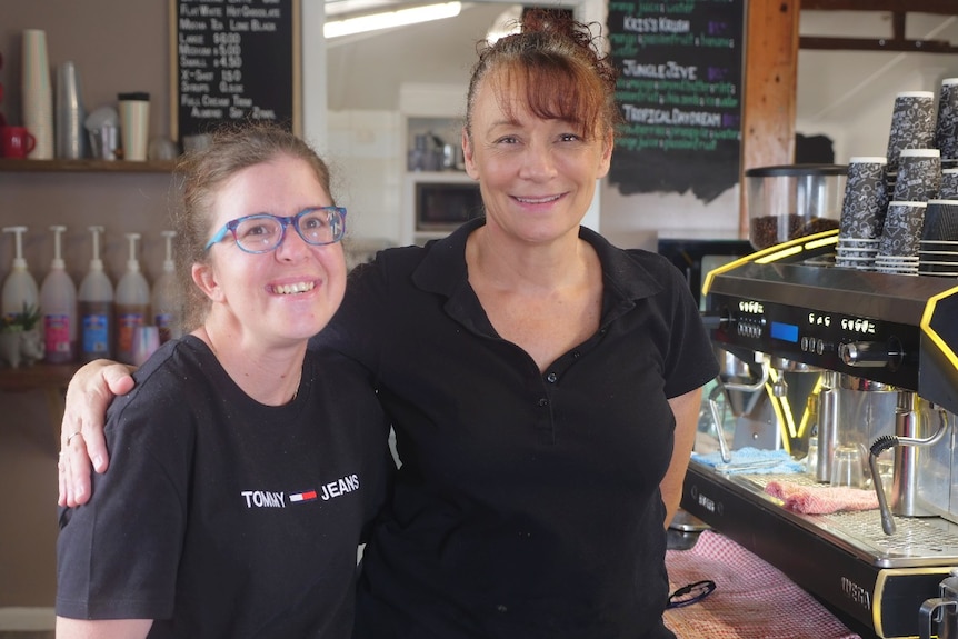 Emily Slotosch, dark shirt, colourful glasses smiling next to Kris Hargrave, dark shirt smiling next to coffee machine.