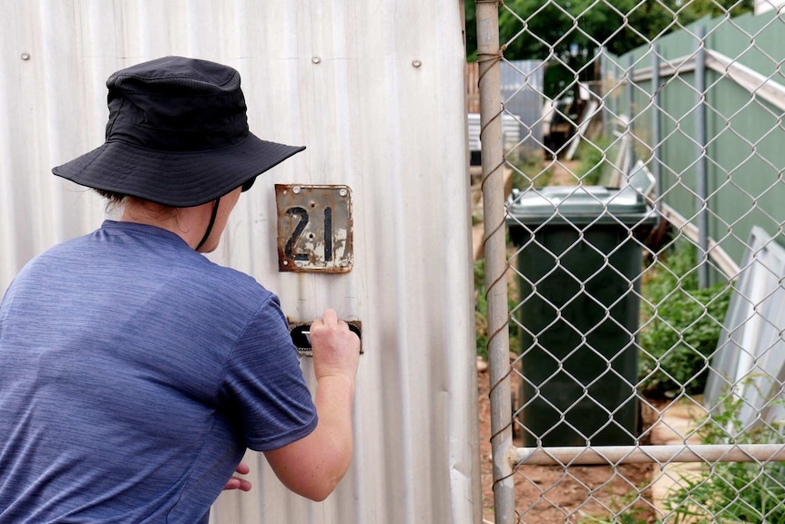 A woman in a hat putting a letter in a mailbox.