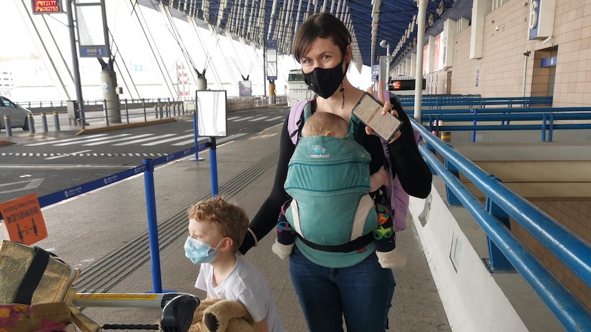 A woman stands outside an airport with her two children.