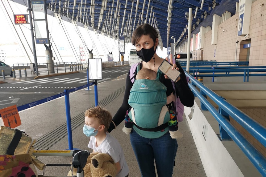 A woman stands outside an airport with her two children.