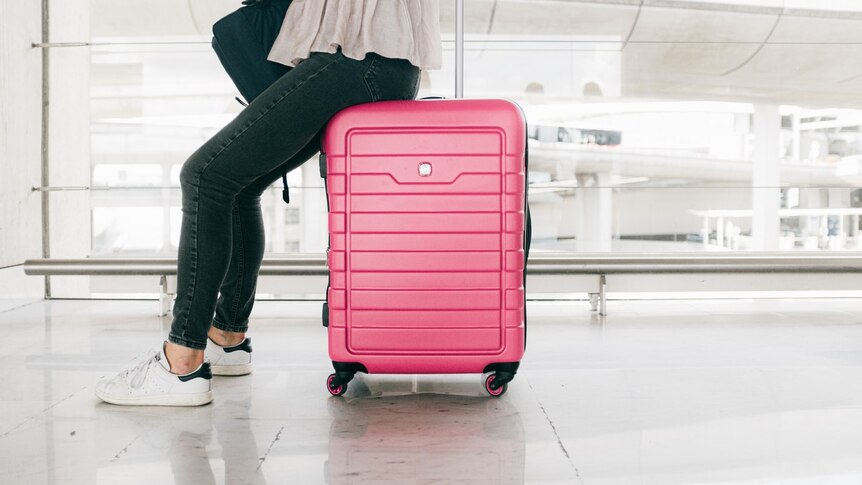 A woman wearing white sneakers sits on a pink suitcase