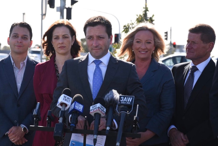 Matthew Guy speaks to reporters in front of a traffic intersection, flanked by his wife and three Liberal candidates.