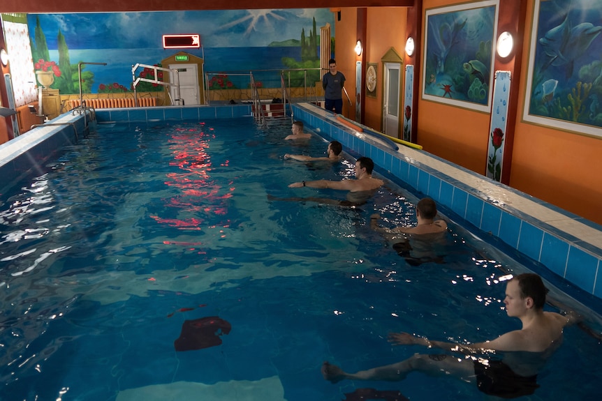 Men line the side of an indoor swimming pool.