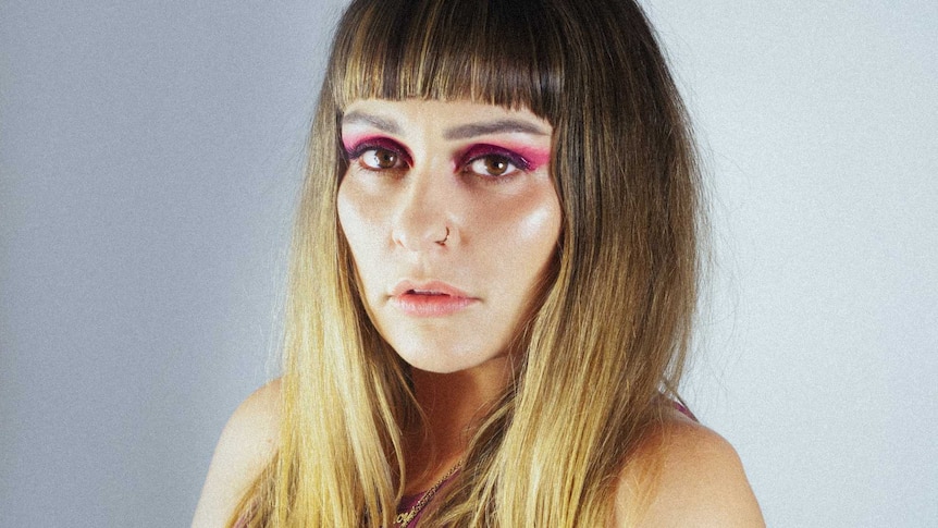 Mincy has balayage brunette to blonde long hair and a fringe & smizes at the camera. She wears pink eyeshadow & pink top.