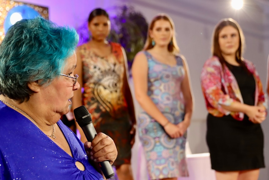 A woman with blue hair talking in front of the models. 