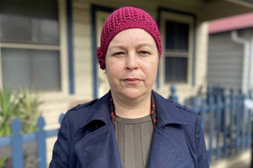 A woman standing outside a house with a maroon beanie on