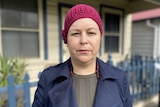 A woman standing outside a house with a maroon beanie on