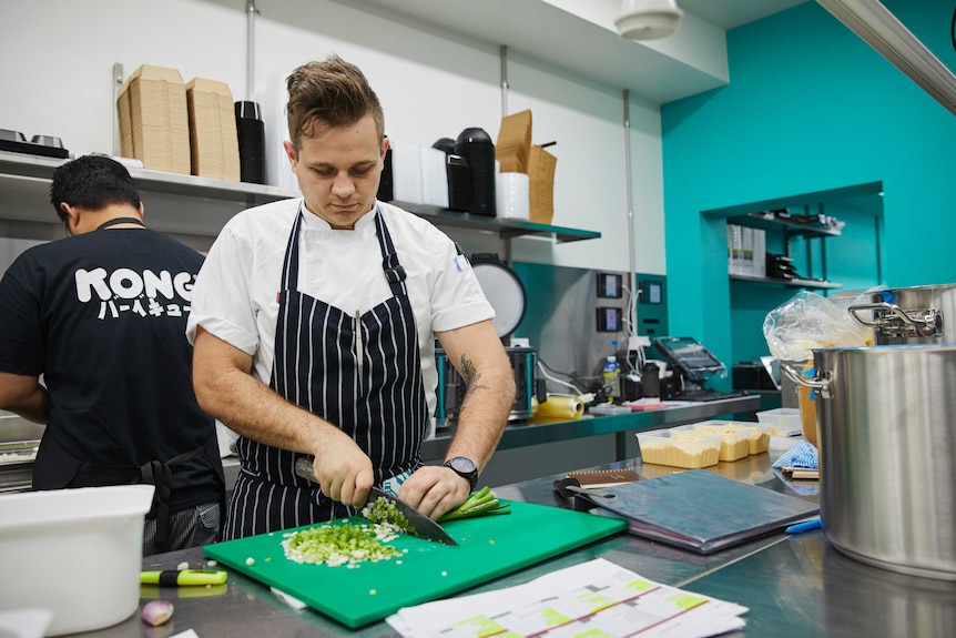 A chef chopping spring onions in a bright commercial kitchen