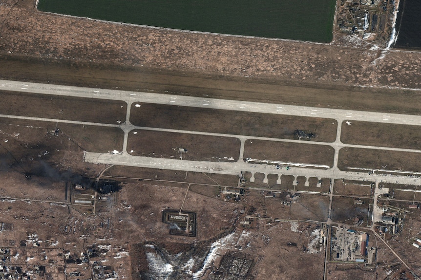 Aerial image shows black smoke arising from a site on the ground at an airfield.
