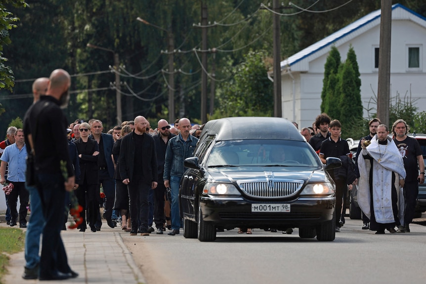 A group of people walk alongside a hearse. 