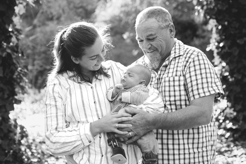 A mother and father hold a baby boy in a black and white family photo