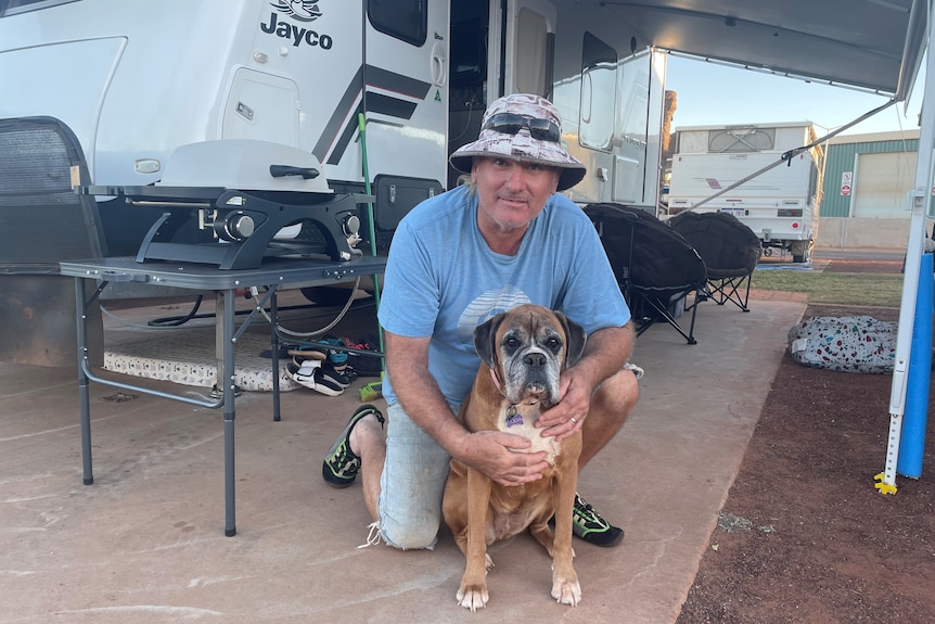 A man and his dog in front of a caravan.
