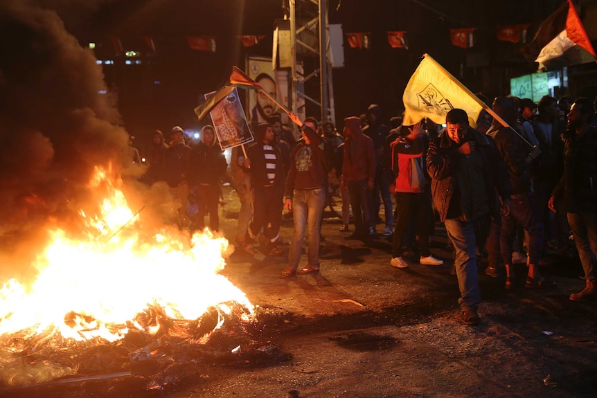 A group of Palestinian protestors burn tires and wave flags around the flames.
