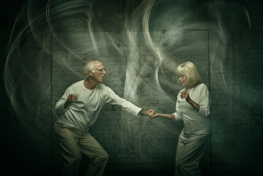 Old man and woman dressed in white holding hands while dancing 