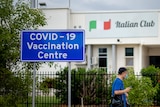 A blue sign reads "COVID-19 vaccination centre" outside a white building