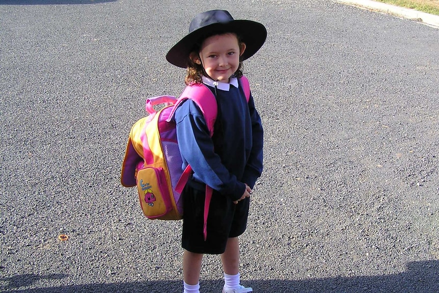 Findlay wears a backpack and her school uniform as she poses in a gravel space ahead of her first day of school.