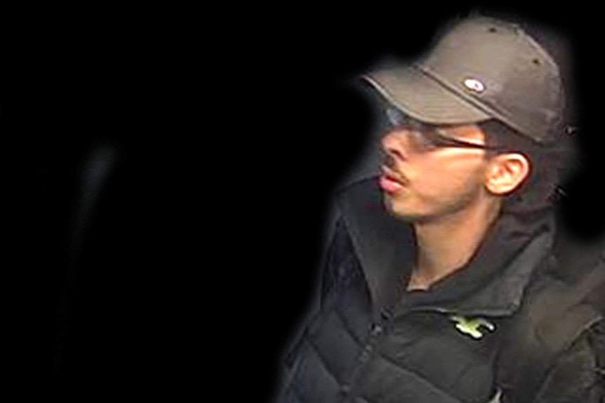 Salman Abedi wears blue jeans, a dark jacket and grey cap. His surroundings have been digitally removed.