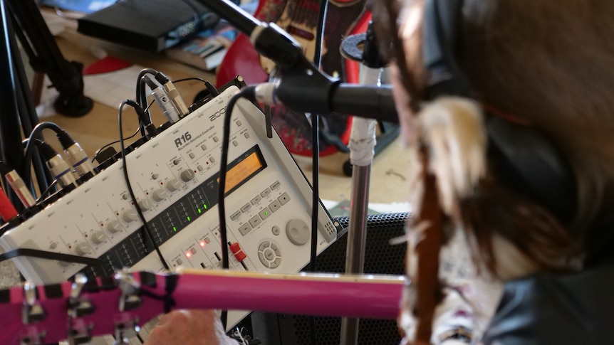 An audio recorder in focus with a musician out of focus recording music in the foreground.
