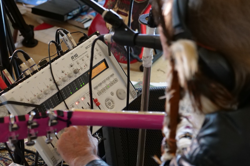 An audio recorder in focus with a musician out of focus recording music in the foreground.