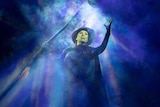 Sheridan Adams as Elphaba. She is holding a broom and surrounded by mist.