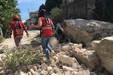 People in red vests walk through rubble of a brick building 