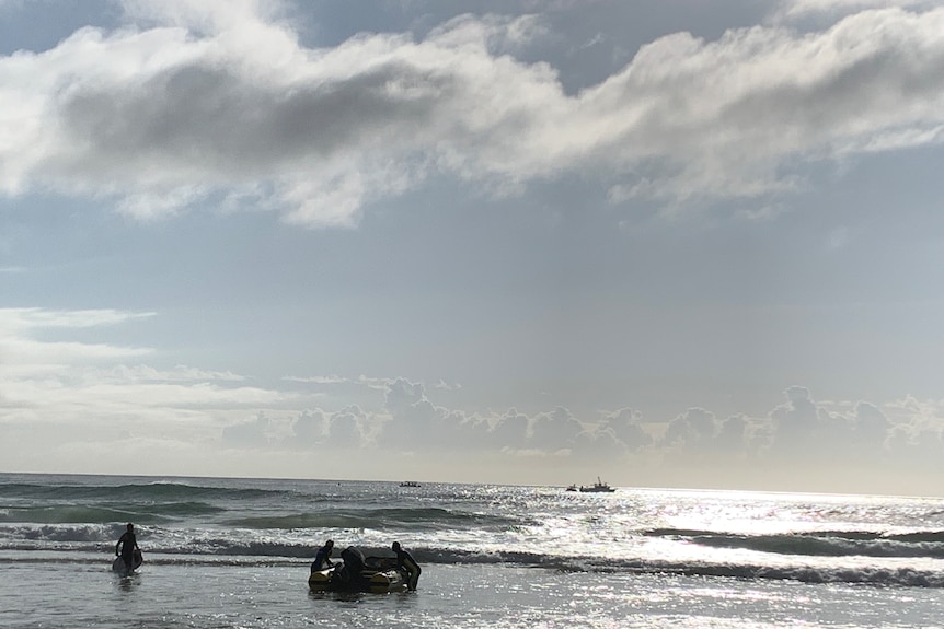 Two men pushing out a small boat into the ocean with silhouette of other boat on horizon.