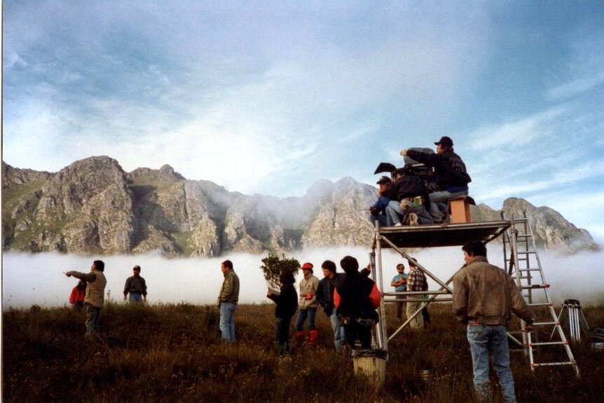 Mountains in background, film crew in foreground, mist hands under mountains