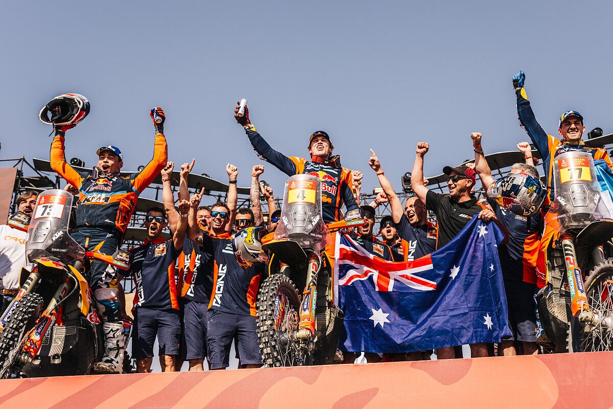 A man on a motorbikes celebrates with a group, and an Australian flag.