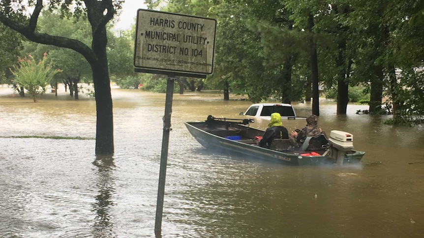Two men steer a small fishing boat down floodwaters.