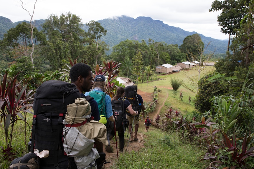 A group of trekkers arrive in a mountainous village, surrounded by trees.