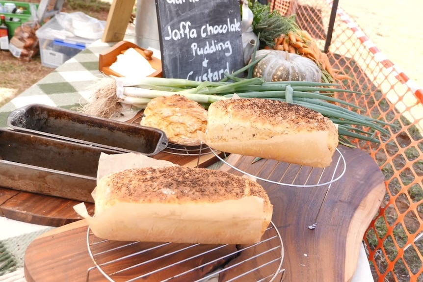 Two loaves of bread sit on a table with veges from a garden