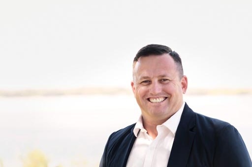 A smiling, dark haired man wearing a dark suit.