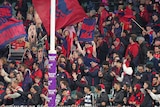 Melbourne AFL fans celebrate in the crowd after their team wins a game.