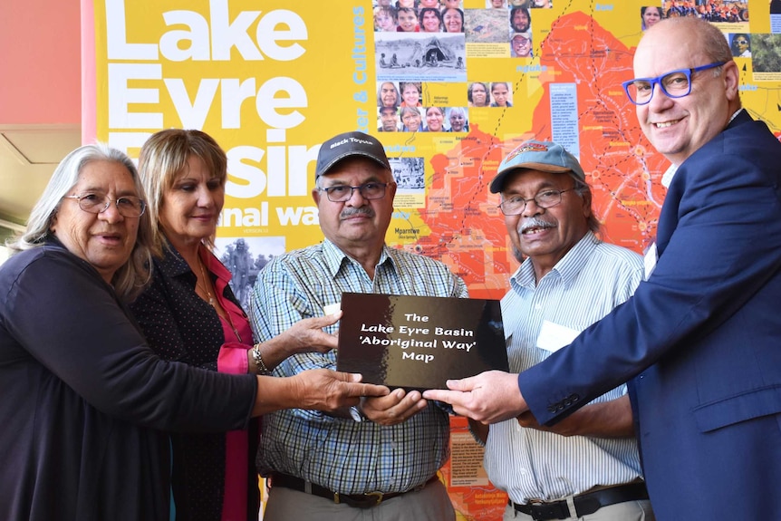 Group of people in front of a large map holding a book looking at the camera.