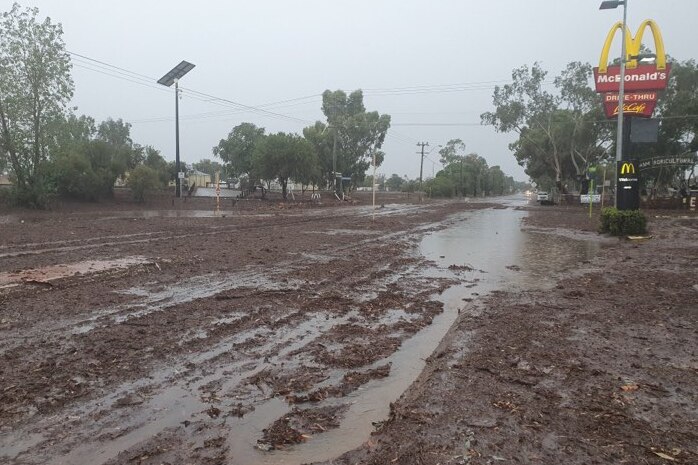 A road is covered in brown mud and water with fast food signage.