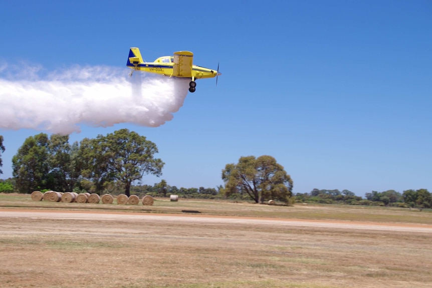 A yellow aeroplane drops a load of water over a stubble paddock