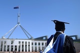 A university graduate wearing a gown and cap is seen outside Parliament House in Canberra