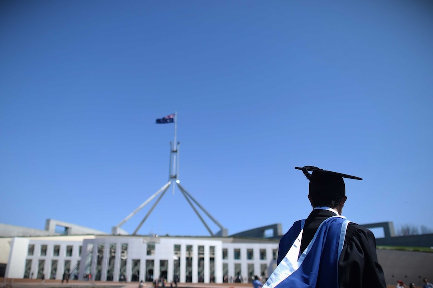 A university graduate wearing a gown and cap is seen outside Parliament House in Canberra