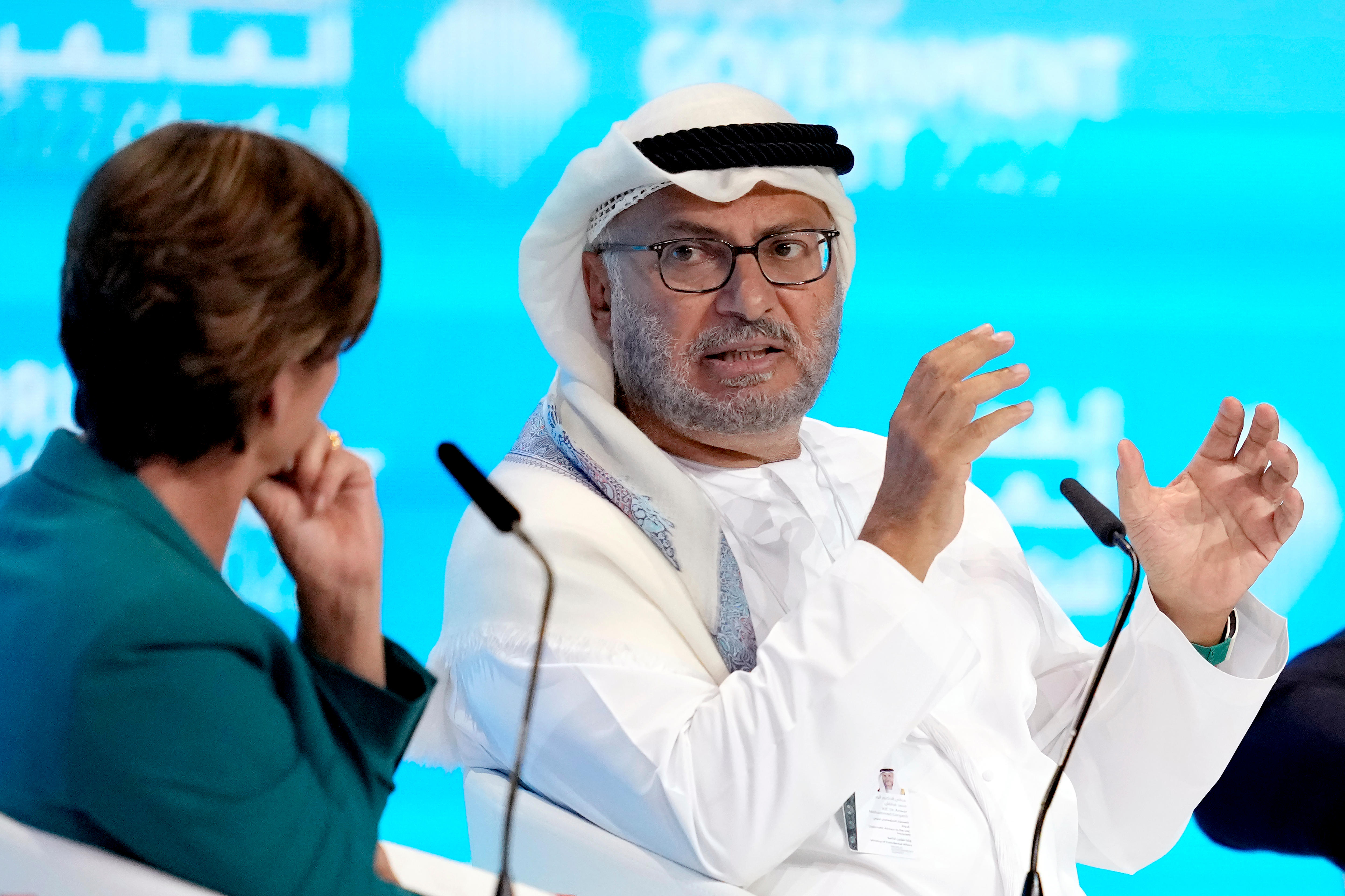 Anwar Gargash sitting behind a microphone, speaking to a person with their back turned on the camera.
