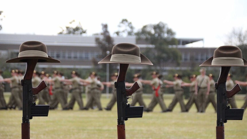 Army slouch hats rest on the stocks of upright rifles