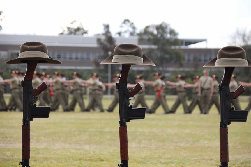 Army slouch hats rest on the stocks of upright rifles