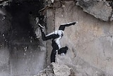 A black and white stencilled graffiti picture of a gymnast on the side of a damaged concrete wall.