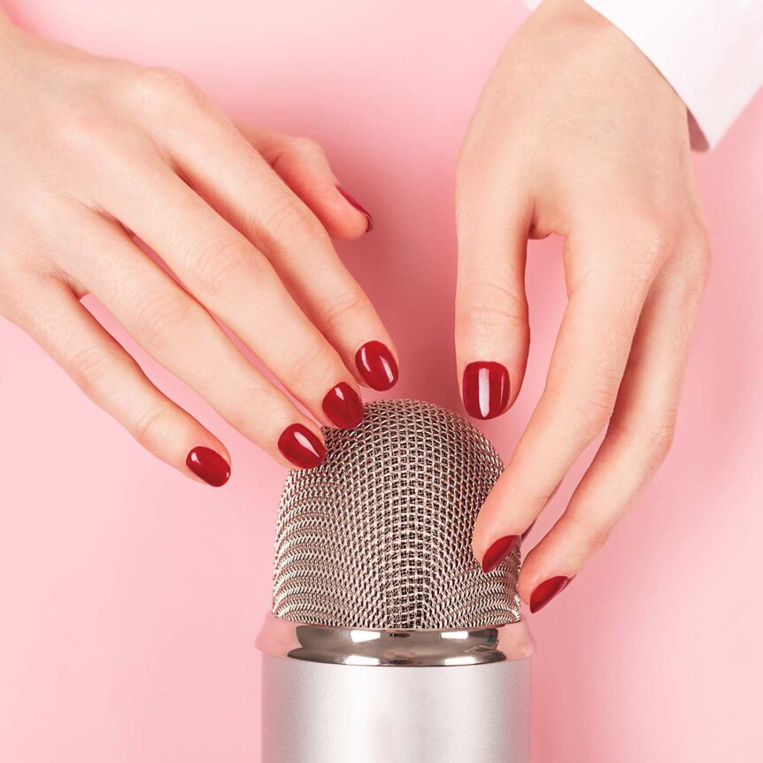 A woman's hands with red fingernails gently touching a microphone